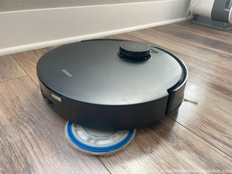 A black t30s robotic vacuum cleaner operating on a wooden floor near a white baseboard.