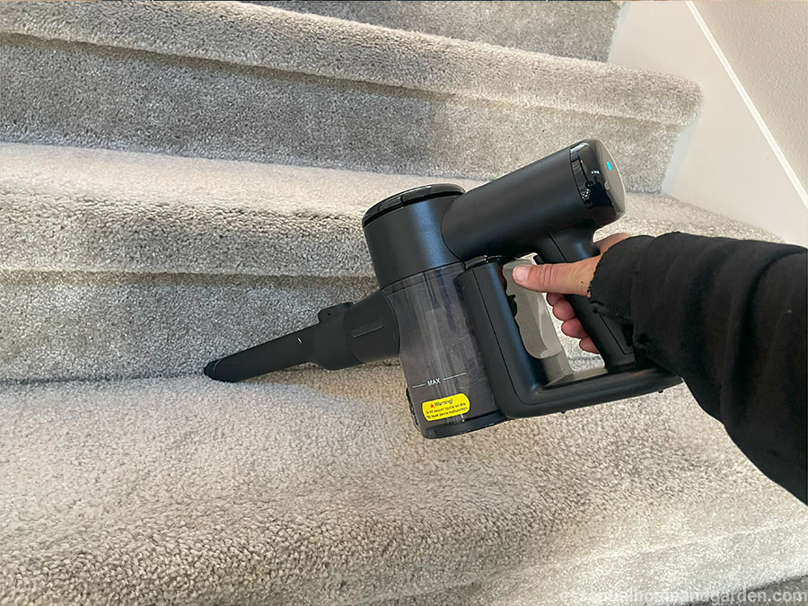 A person holding a cordless handheld vacuum cleaner on a gray carpeted staircase.