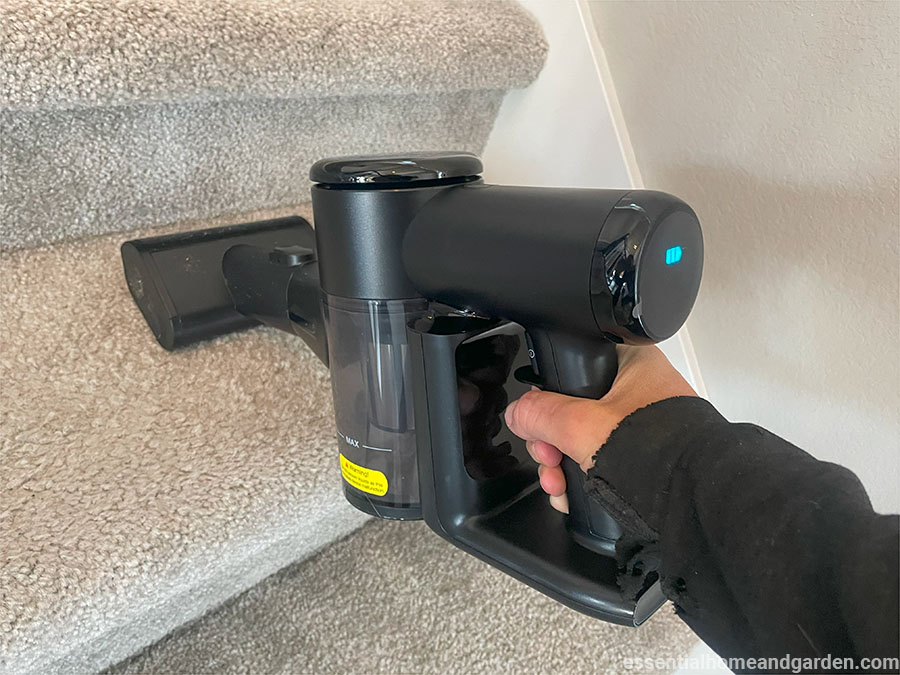 A person using a handheld vacuum cleaner to clean grey carpeted stairs.